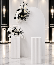 Load image into Gallery viewer, White arch backdrop, 2 x black &amp; white flowers, 2 x white square ripple plinths - HIRE ONLY
